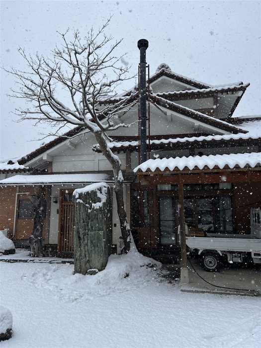 雪化粧した古民家と薪ストーブの煙突