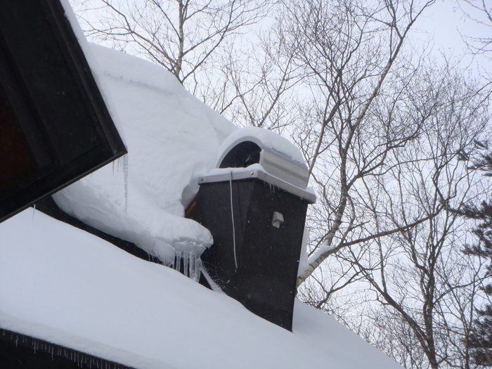 厚い雪に埋もれた屋根と煙突、軒下に下がる長いつらら。岩手の厳冬