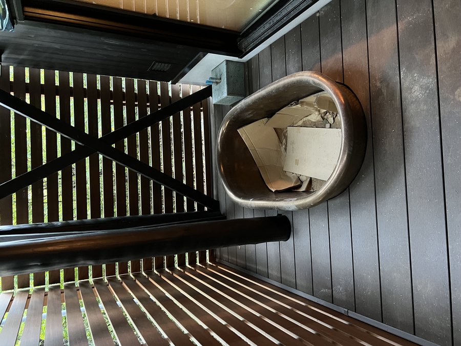 当社施工:黒い外壁のサウナ小屋の前、木のデッキに置かれた水風呂用のバスタブ