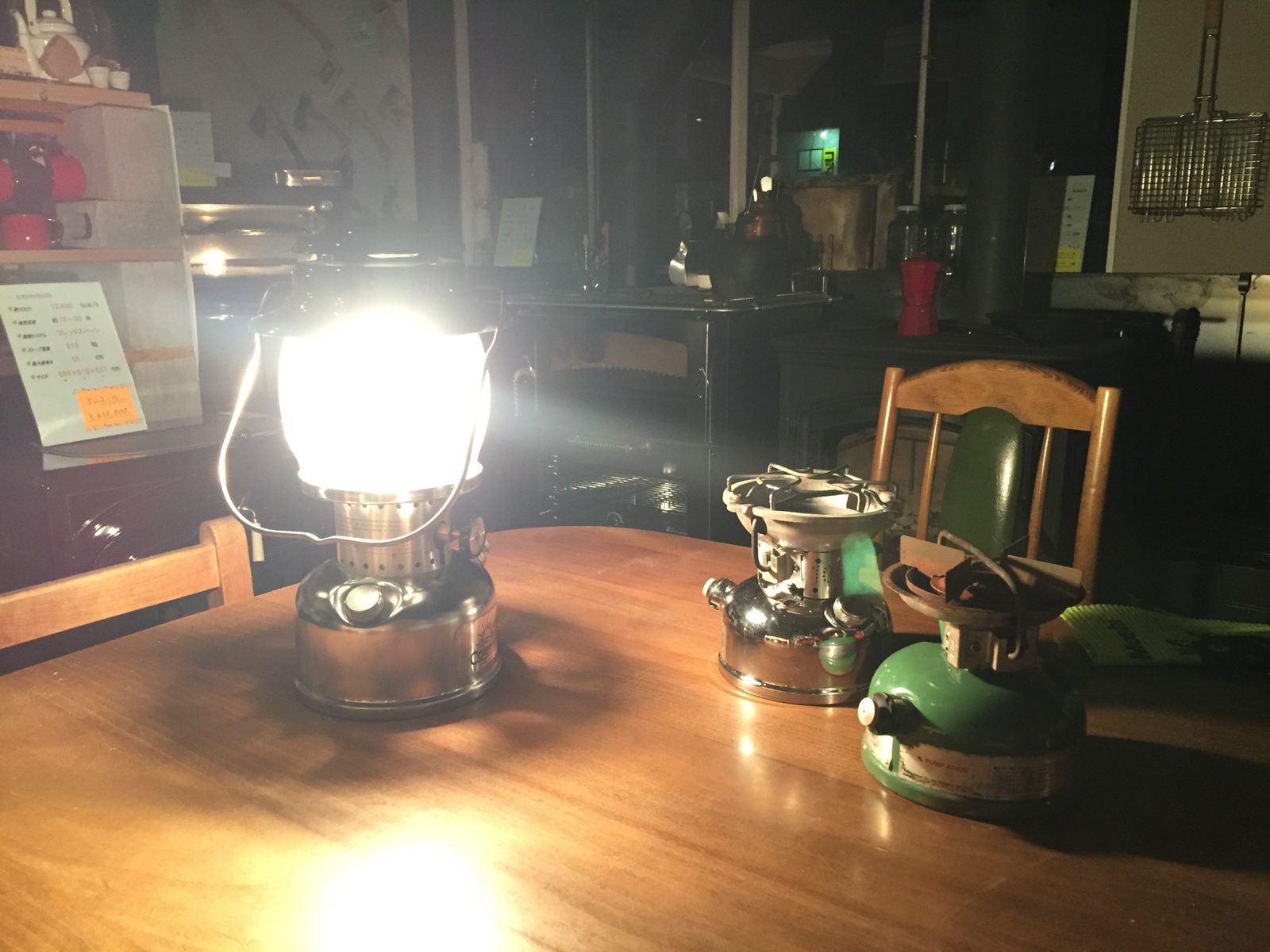 夜の工房。直したコールマンのランタンが灯り、隣にレストアを終えたストーブが2台並ぶ